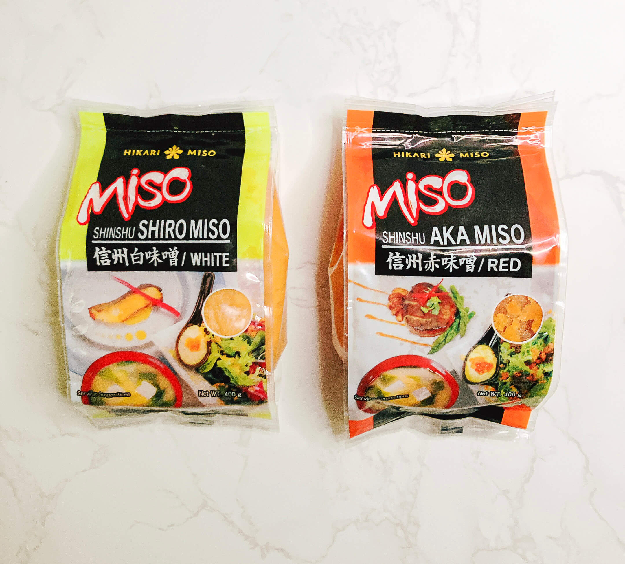 Front view of packaged white miso and red miso paste placed side by side on a white background