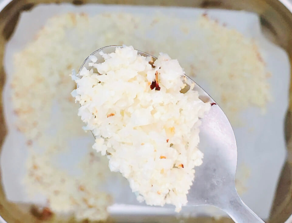 Oven-baked cauliflower rice on a spoon, showing fluffy grains with light golden edges.”