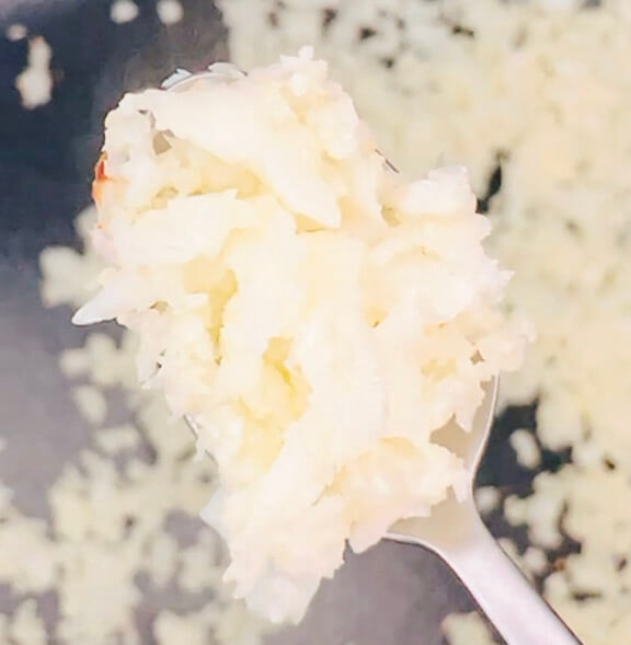 Pan-fried cauliflower rice on a spoon, showing fluffy grains with light golden flecks