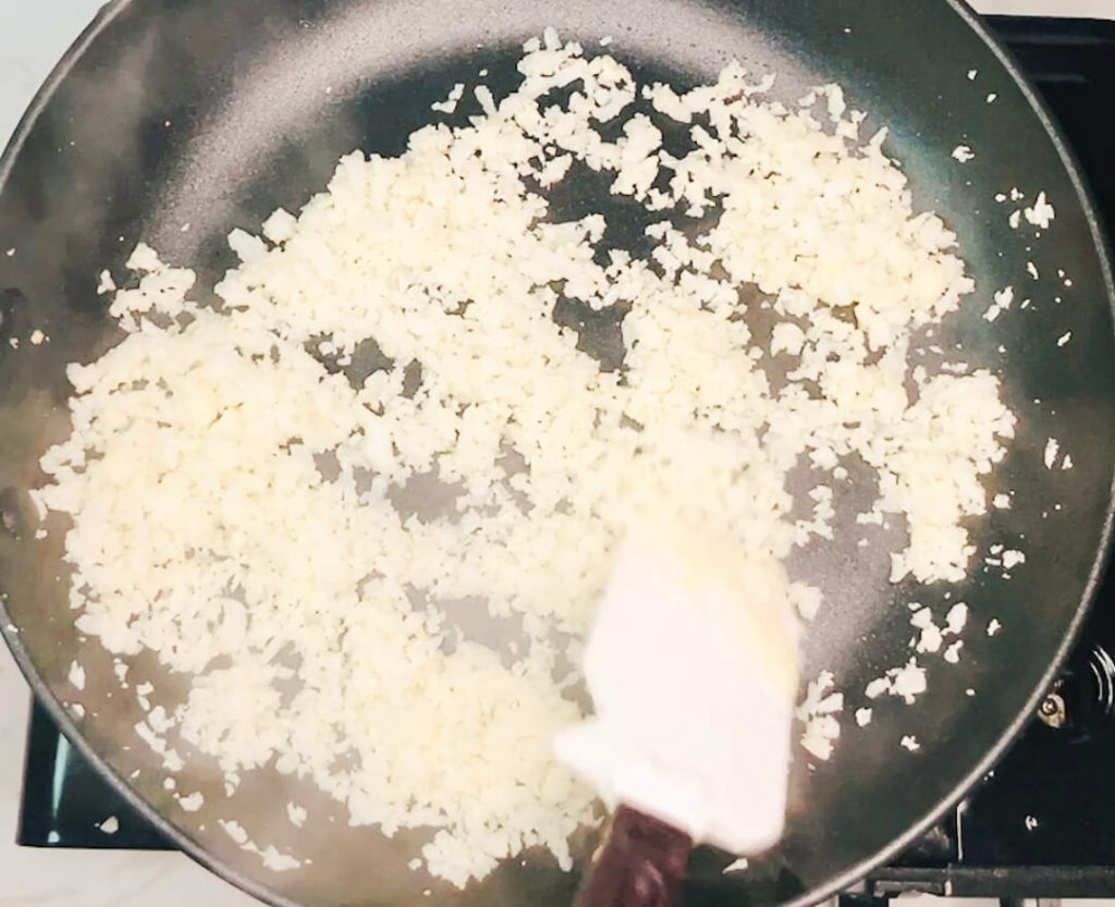 Cauliflower rice cooking in a skillet, partway through the pan-frying method.