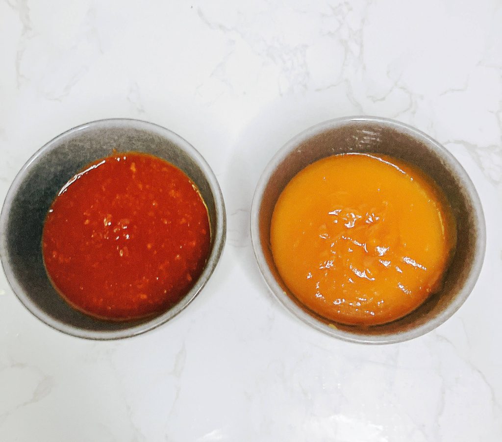 Top-down view of red miso sauce and white miso sauce side by side in small glass bowls on a white background