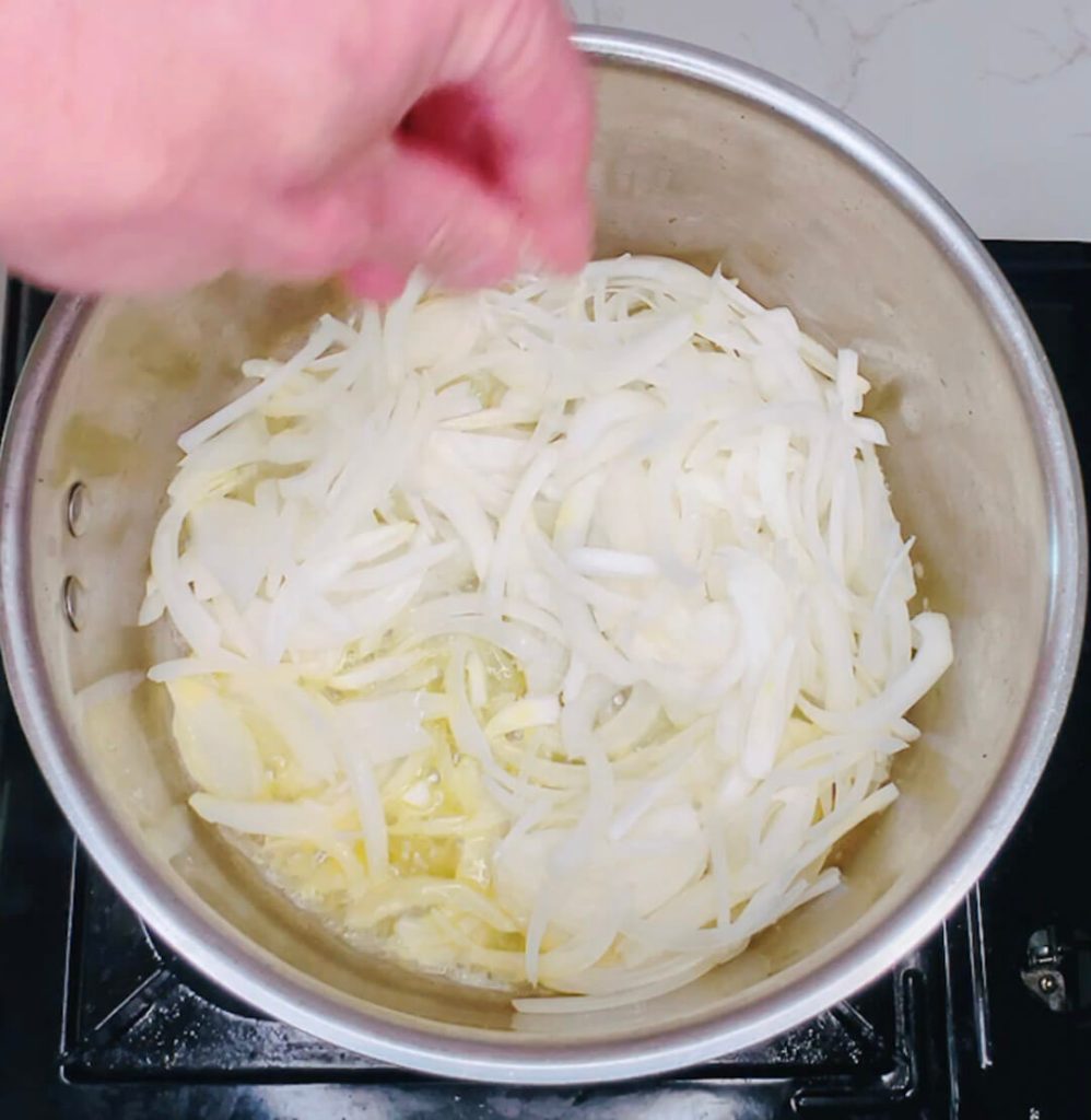 Seasoning sliced onions with salt in a saucepan for keto chicken katsu curry.