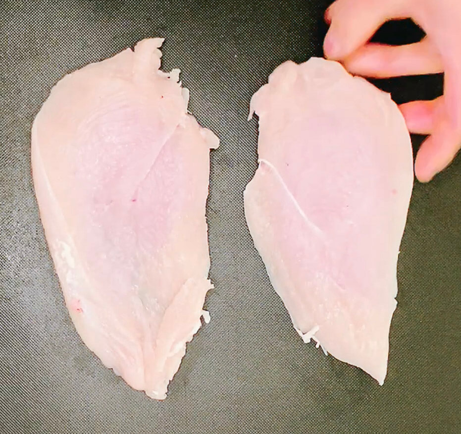 Cutting raw chicken breast in half for keto chicken katsu.