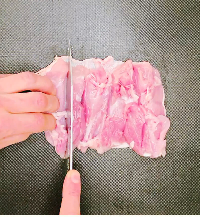 Cutting a chicken thigh open with a knife to prepare for marinating.