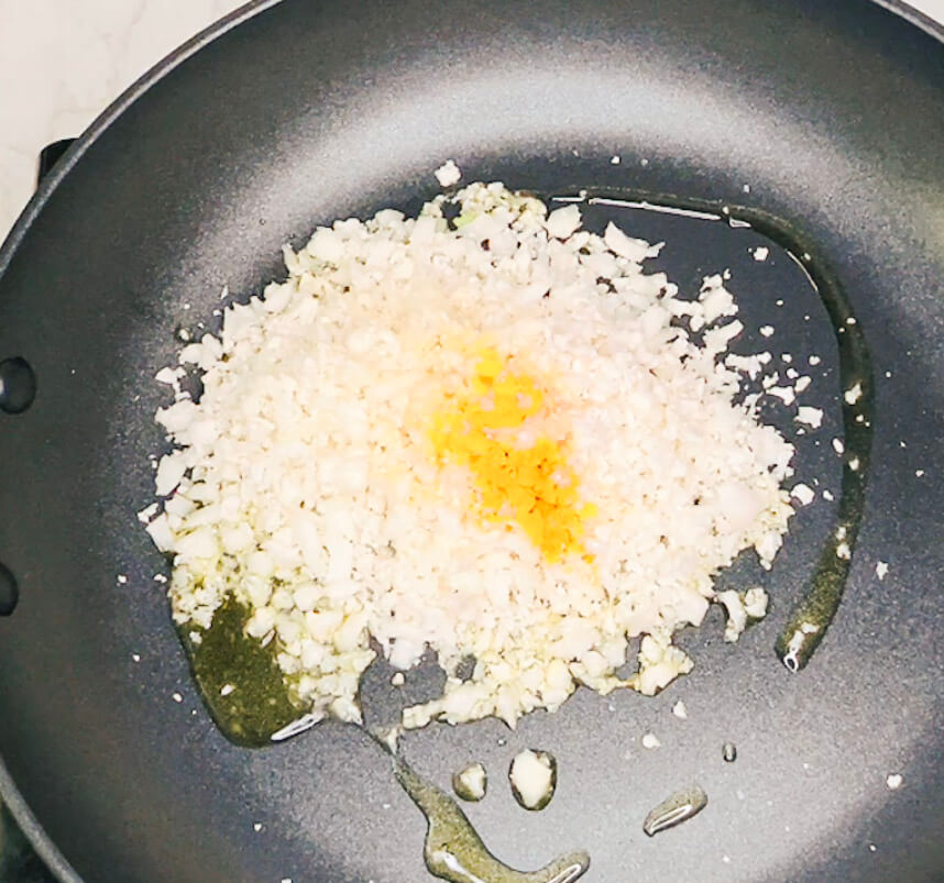 Cauliflower rice in a pan with turmeric, garlic powder, and salt before stirring.”