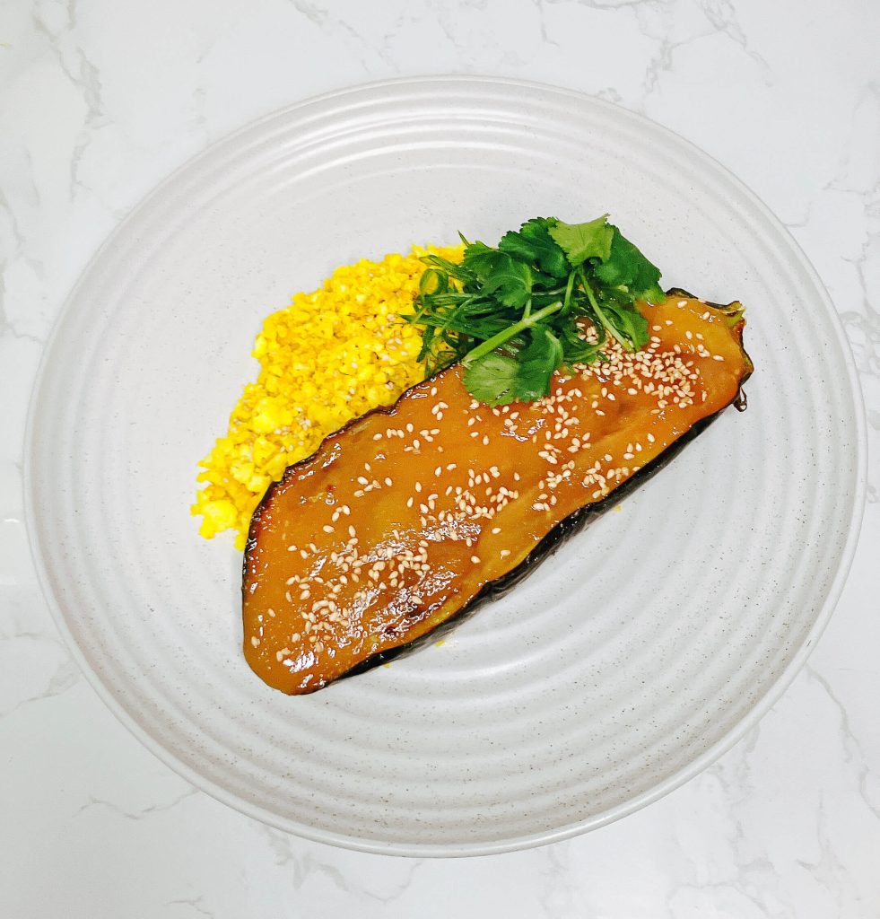 White miso-glazed eggplant served with turmeric cauliflower rice, garnished with fresh herbs, on a white plate.