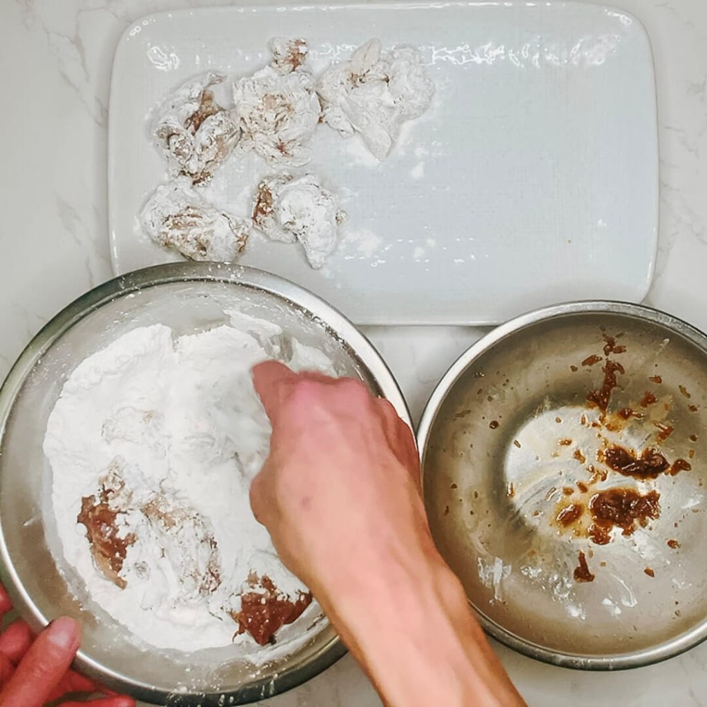 Hand dredging marinated chicken pieces in potato starch for karaage chicken.