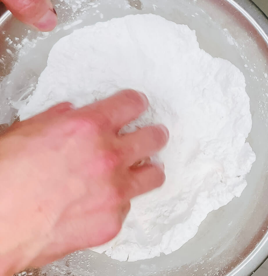 Hand coating chicken pieces in potato starch for the second coating of karaage chicken."