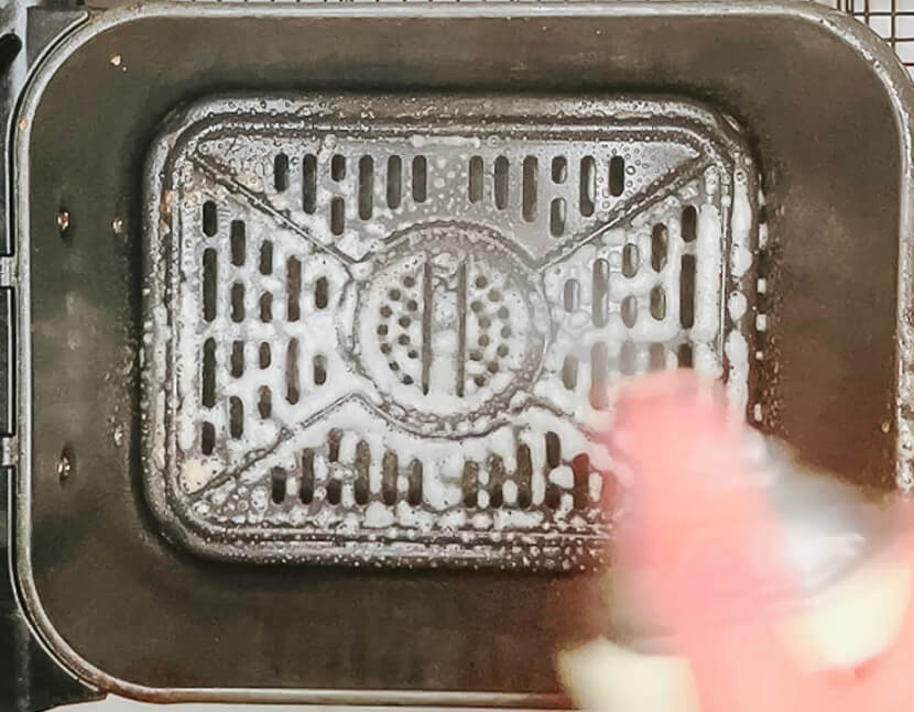 "Hand oiling a preheated air fryer basket before cooking karaage chicken."