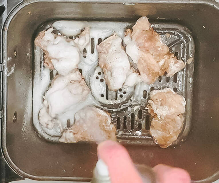 Lightly spraying oil over karaage chicken pieces in the air fryer basket after flipping halfway through the first fry