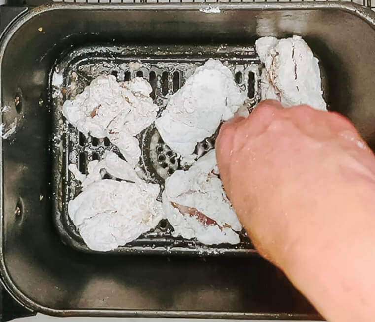 Hand placing coated karaage chicken pieces into a preheated, oiled air fryer basket