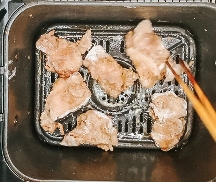 Coated karaage chicken pieces being flipped halfway through the first air fry.