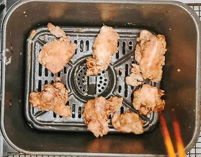 Coated karaage chicken pieces being flipped in the air fryer basket halfway through the second fry