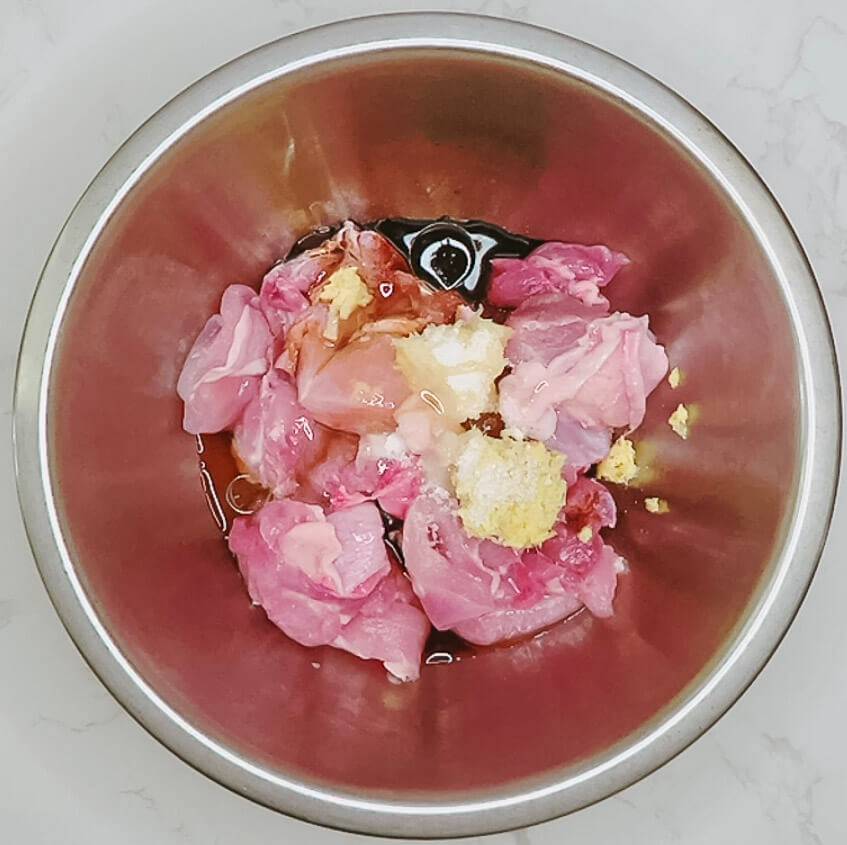 Chicken thigh pieces in a bowl with tamari, sake, ginger, garlic, oil, salt, and sugar for karaage marinade