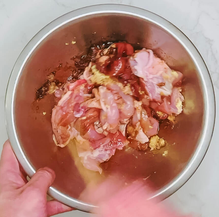Hand mixing chicken thigh pieces with tamari, sake, ginger, garlic, oil, salt, and sugar for karaage chicken