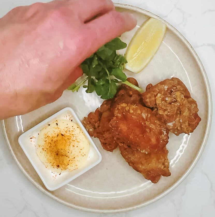 Karaage chicken plated with dipping sauce, watercress, and lemon wedge before adding cucumber pickles.