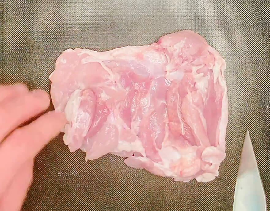 Raw chicken thigh prepared for karaage chicken, placed on a cutting board."