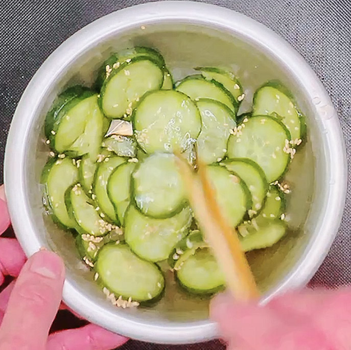 Hand mixing cucumber slices with sesame seeds and seasonings for quick Japanese pickles.