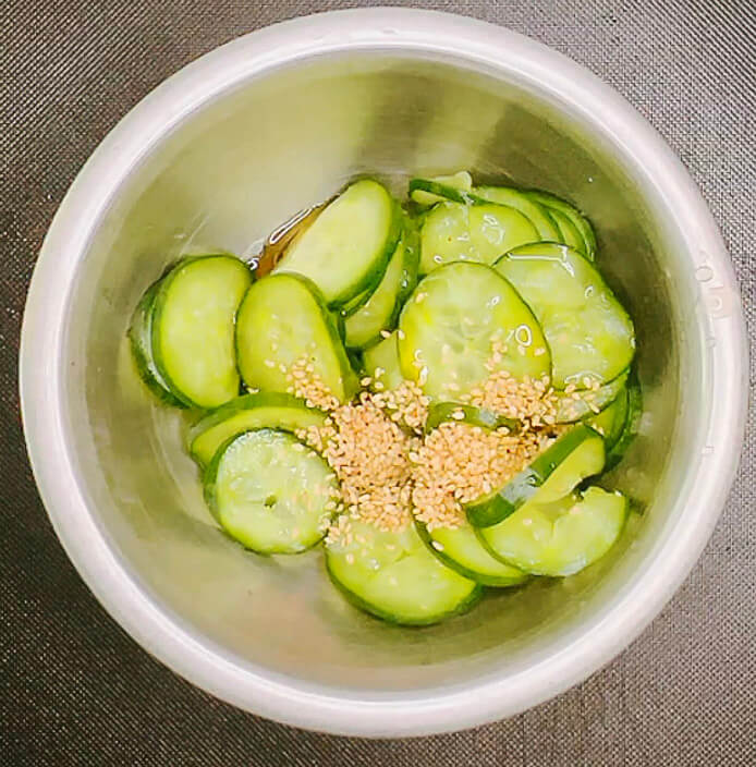 Squeezed cucumber slices in a bowl with sesame seeds and seasoning for quick pickles