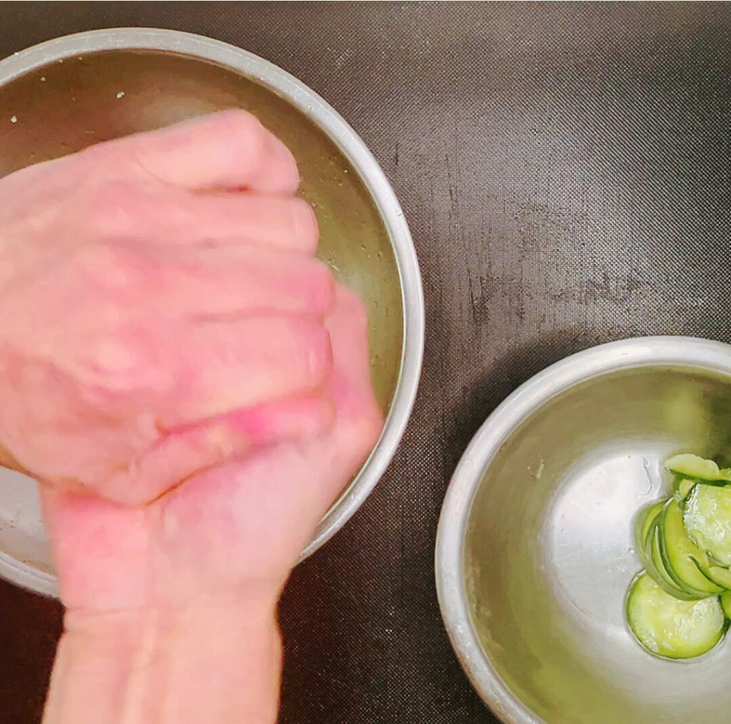 Hand squeezing salted cucumber slices to remove excess liquid.