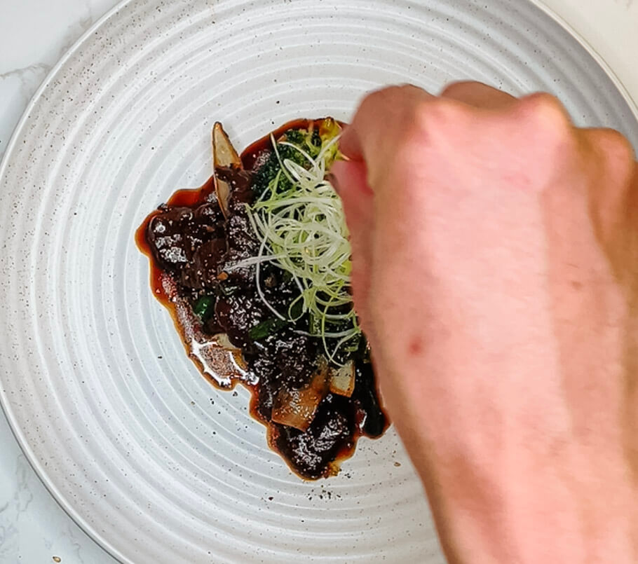 Adding fresh scallions as the final garnish to black pepper teriyaki beef before serving.