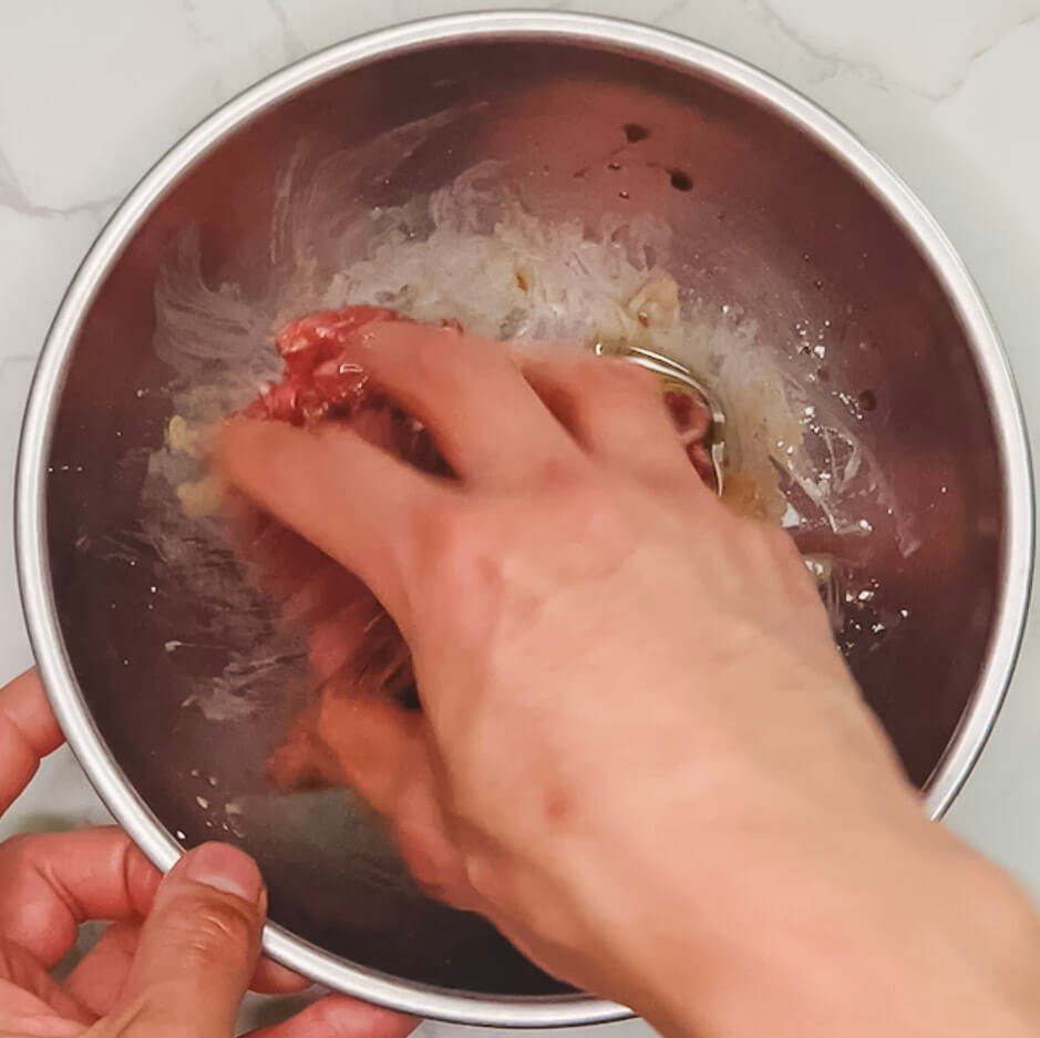 final mixing of marinated beef showing glossy, evenly coated slices for black pepper teriyaki beef.