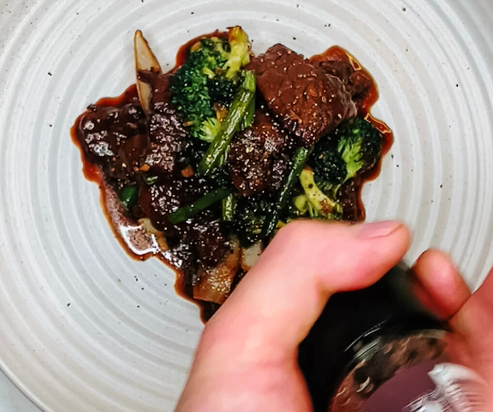 Adding final seasoning and garnish to black pepper teriyaki beef before serving.