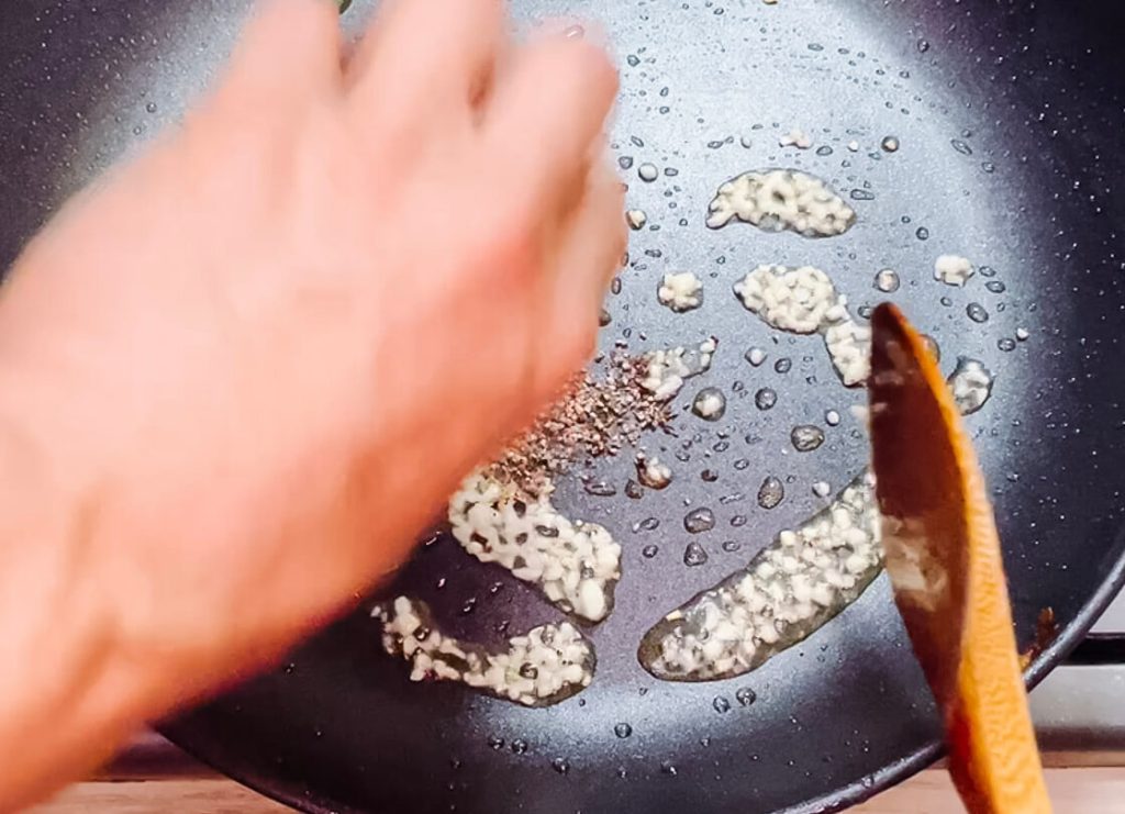 Sautéing minced garlic and crushed black pepper in a pan for black pepper teriyaki beef.