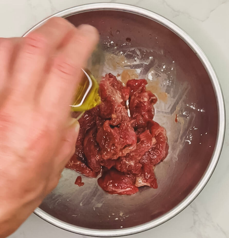 adding oil to marinated beef to seal the coating for black pepper teriyaki beef.
