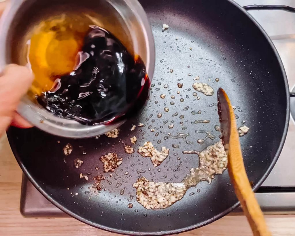 Pouring teriyaki sauce into the pan with garlic and pepper for black pepper teriyaki beef.