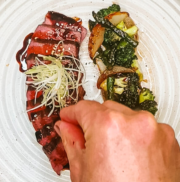 Garnishing sliced teriyaki steak with sprouts and vegetables for black pepper teriyaki beef.