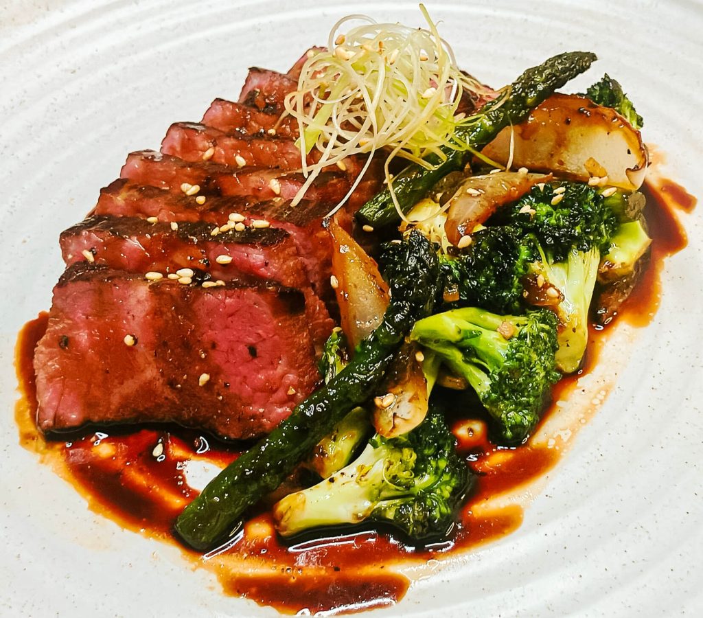 Black pepper teriyaki beef steak with asparagus and broccoli, glazed with glossy teriyaki sauce on a white plate