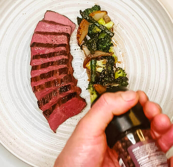 Finishing the black pepper teriyaki steak with freshly ground black pepper and glaze.