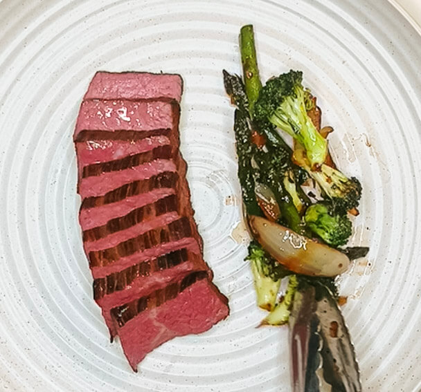 Sliced steak plated with glazed asparagus and broccoli for black pepper teriyaki beef.