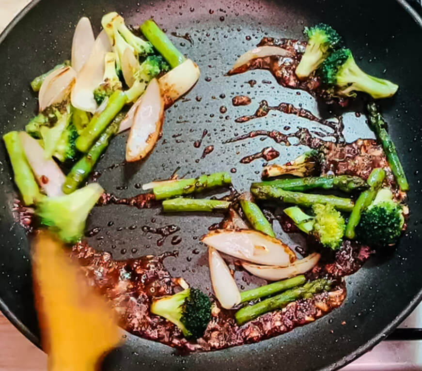 Asparagus and broccoli simmering in teriyaki sauce while steak rests nearby for black pepper teriyaki beef.