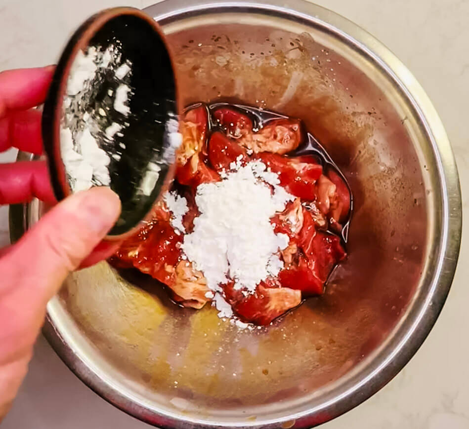 Mixing marinated pork with cornstarch in a red bowl to form a thin, even coating before air frying.