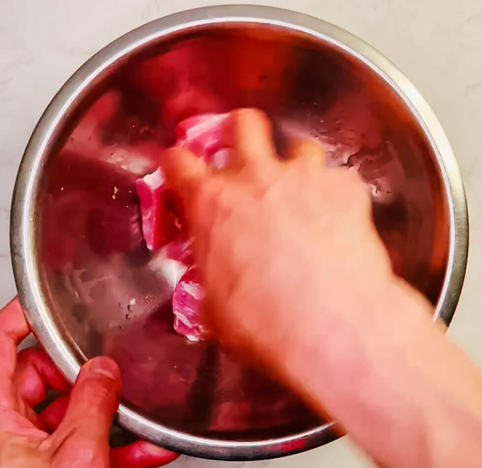 Raw pork pieces marinating in a red bowl with water and baking soda mixture for tenderizing before air-frying.
