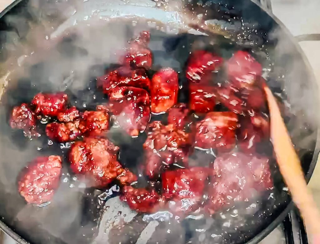 Crispy air-fried pork pieces being coated in glossy red sweet and sour sauce in a frying pan.