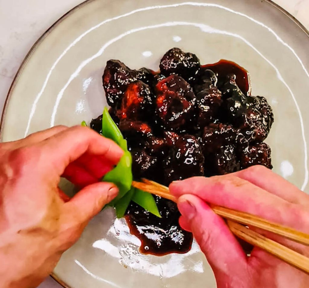 Adding garnish to the plated sweet and sour pork, finishing the dish with a fresh and colorful touch.