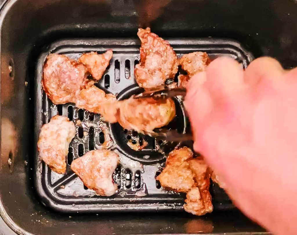 Flipping pork pieces in the air fryer basket during the second fry to ensure deep golden color and even crisping.