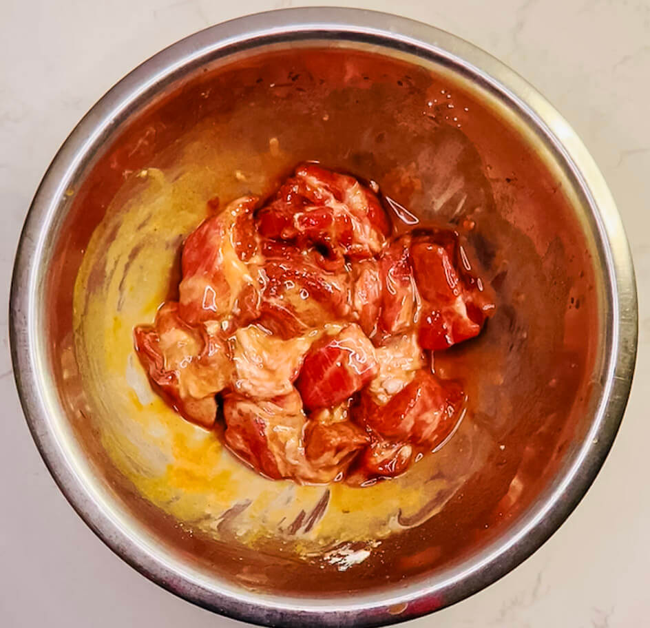 Marinated pork coated with cornstarch in a red bowl, ready to be air-fried for sweet and sour pork.
