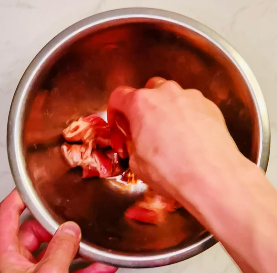Mixing pork thoroughly with egg, soy sauce, and seasonings in a red bowl before coating with starch for air fryer sweet and sour pork.