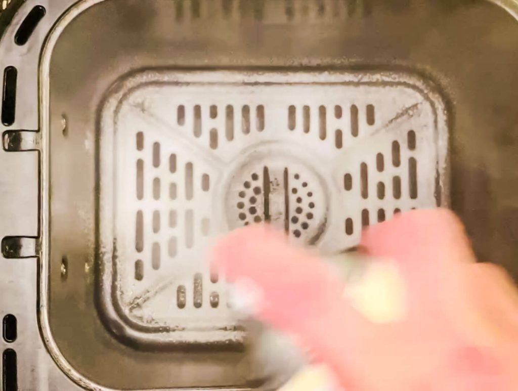 Spraying oil on the air fryer basket before cooking sweet and sour pork to prevent sticking and promote even browning.