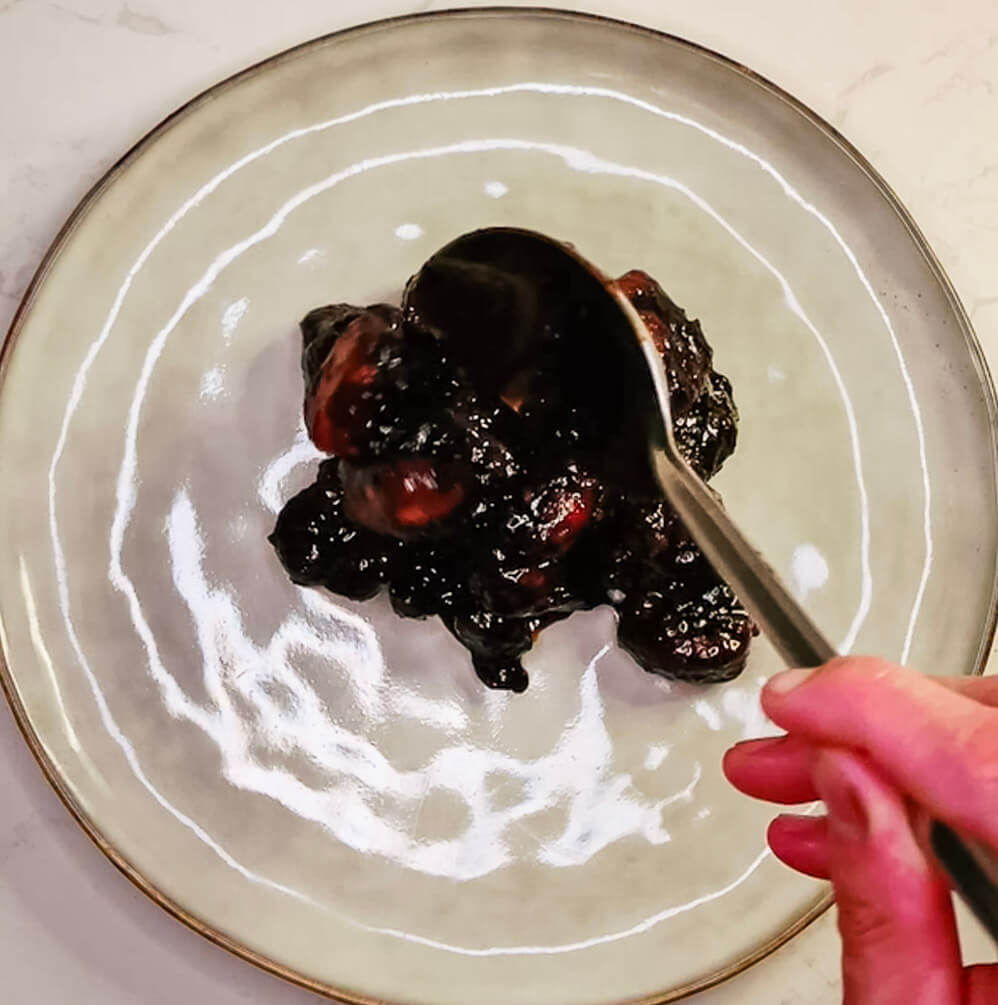 Plating glossy sweet and sour pork onto a white serving plate using tongs.
