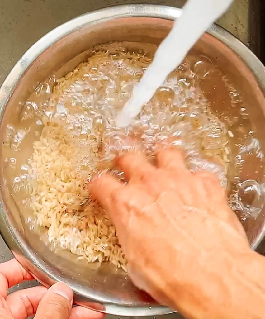 Washing brown rice in a bowl to remove excess starch before cooking