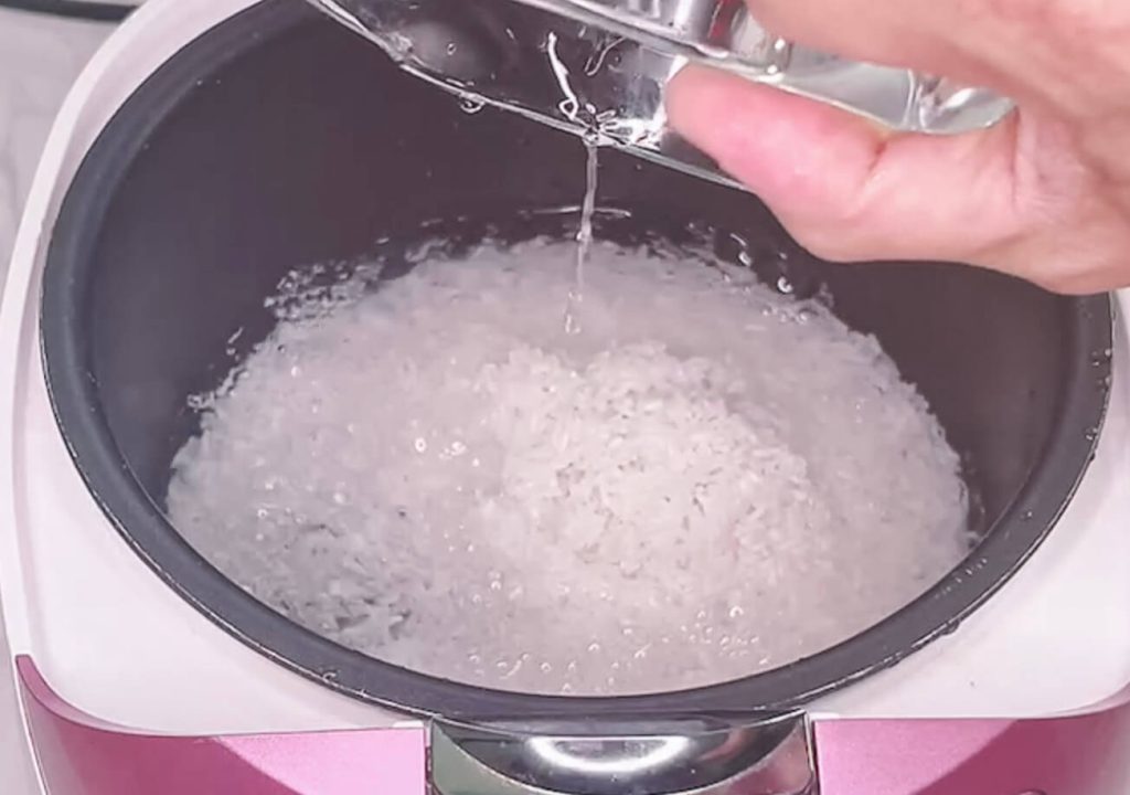 Adding water to washed white rice in a rice cooker bowl