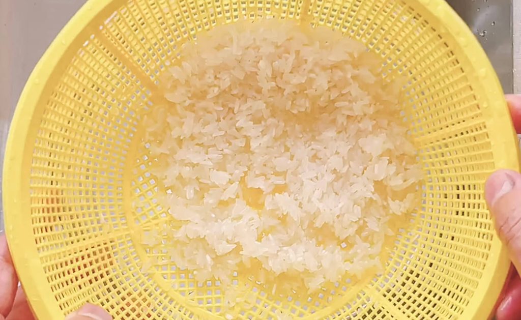 Washed white rice drained in a strainer and ready to cook
