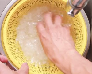 washing white rice by hand in a colander to remove excess starch