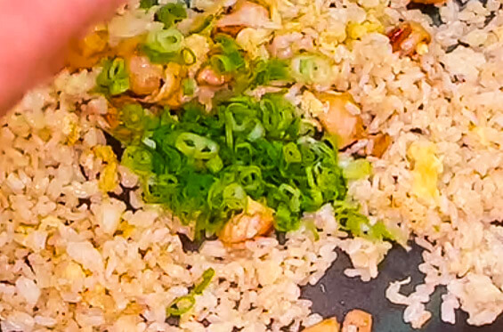 Adding chopped spring onion to chicken fried rice in pan