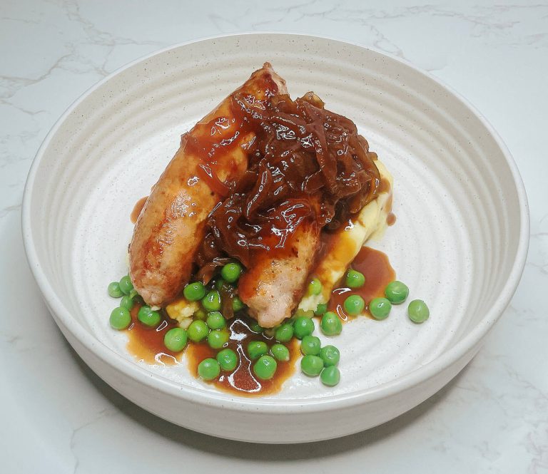 Alt Text: Bangers and mash with sausages, peas, and teriyaki onion gravy on a white plate